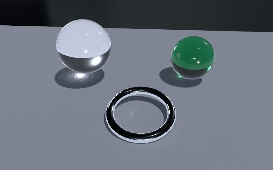 Two glass spheres and a chrome ring on a sunlit matte table. The clear sphere throws a tight bright spot inside its own shadow, the bottle-green sphere throws a green-tinted one, and the ring, lying almost flat, folds light into a radial fan across its middle