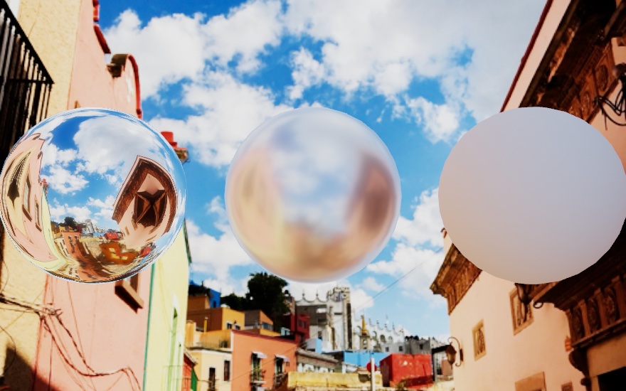 Three spheres floating in front of a photograph of a narrow street under a bright cloudy sky. The chrome sphere on the left carries the whole street wrapped around it, buildings and clouds and all, the middle sphere smears the same reflection into a satin sheen, and the white matte sphere on the right just takes the daylight