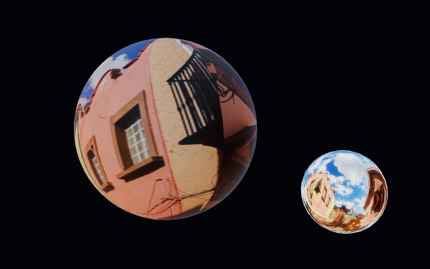 A large sphere wrapped in the same street photograph as the figure above, a pink wall and its window and balcony wrapped around the globe, beside a small chrome ball reflecting the same street. Both are lit by the picture they show